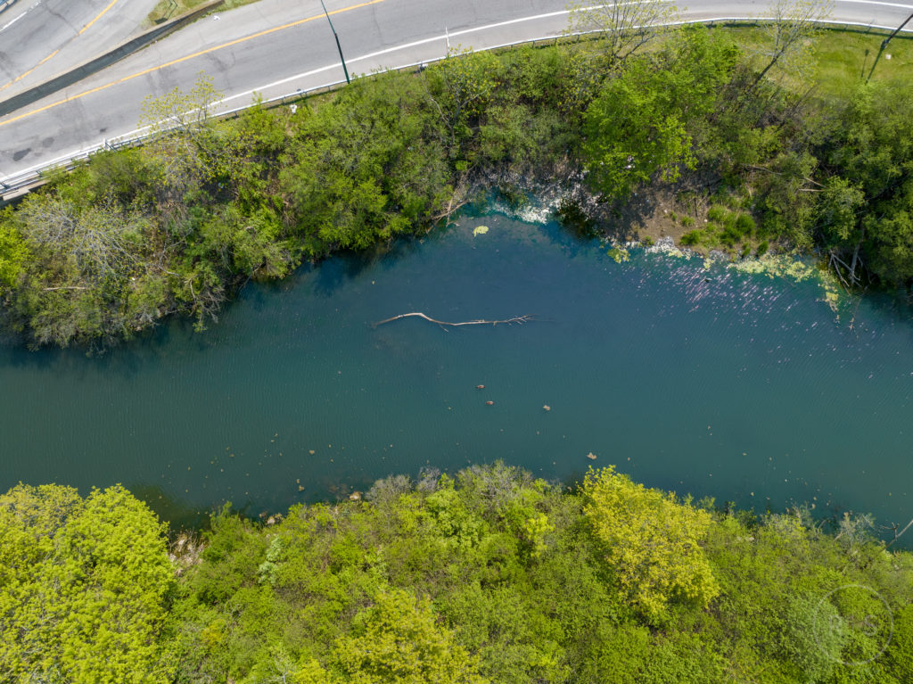 Aerial perspective of Scajaquada Creek, flowing parallel to the New York State Route 198, providing a contrast between the natural waterway and the nearby man-made transportation infrastructure.